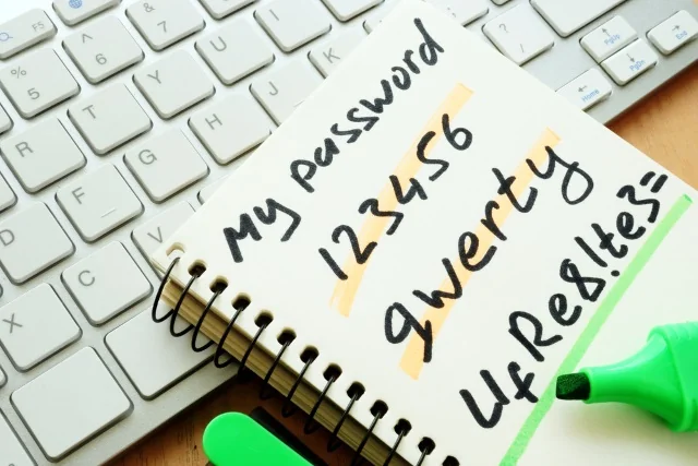 Bloc de notas con contraseñas manuscritas "123456" y "qwerty" en el teclado.