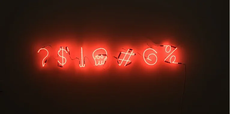 Red neon lights display symbols in a dark setting: ?, $, skull, #, %Z. The glowing letters create a mysterious ambiance.